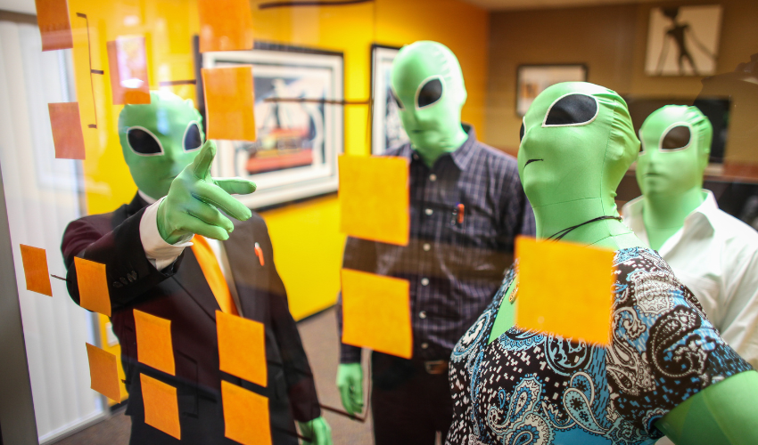 employees wearing alien masks together reviewing whiteboard