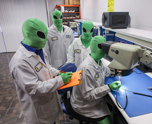area51 electronics employees wearing lab coats and alien masks performing quality checks